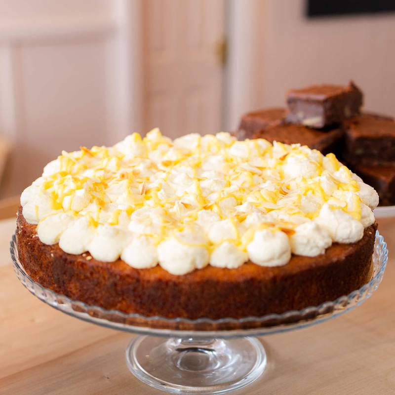 A lemon cream cake on a glass stand with brownies behind